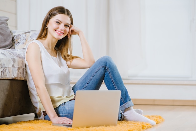 Feliz mulher jovem ou estudante com laptop sentado no chão em casa