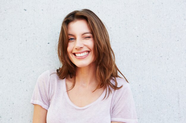 Foto feliz, mulher jovem, sorrindo, e, piscando, contra, parede cinza