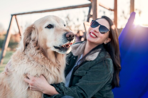 Feliz mulher latina sentada ao ar livre e sorrindo ao lado de um cão retriever no retrato de plyagroundx9