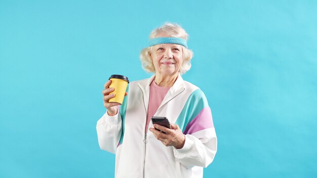 Feliz mulher madura com cabelos grisalhos com um agasalho verifica a notificação em um smartphone moderno.