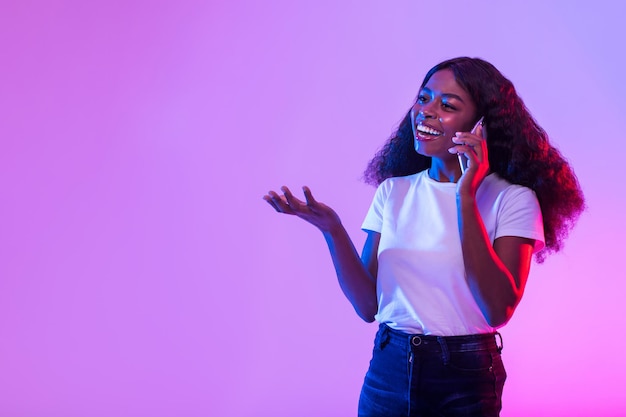 Feliz mulher negra milenar falando no smartphone em espaço livre de luz neon