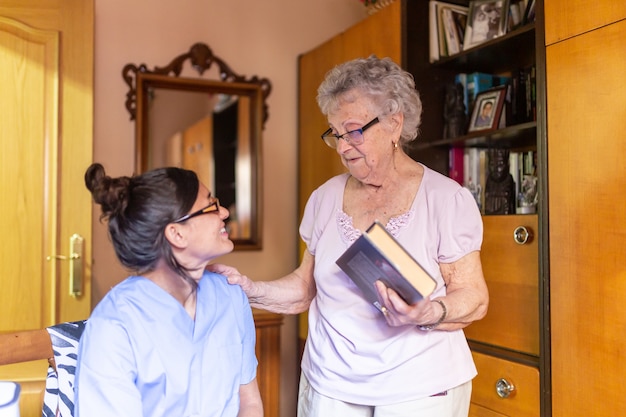 Feliz mulher sênior com seu cuidador em casa segurando um livro