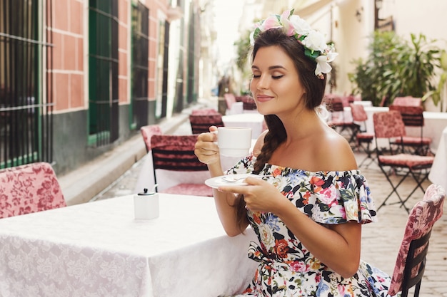 Feliz mulher sentada no café rua com uma xícara de café quente