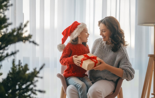 Feliz Natal, Boas Festas. Mãe alegre e sua linda filha trocando presentes. Pai e filho se divertindo perto da árvore dentro de casa.