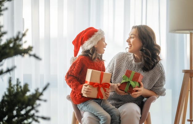 Feliz Natal, Boas Festas. Mãe alegre e sua linda filha trocando presentes. Pai e filho se divertindo perto da árvore dentro de casa.