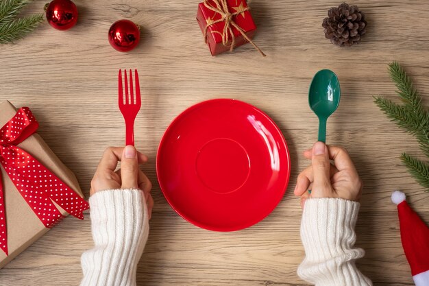 Feliz Natal com a mão de uma mulher segurando o prato, o garfo e a colher no fundo da mesa de madeira. Conceito de Natal, festa e feliz ano novo