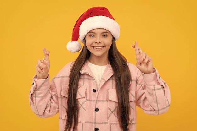 Feliz natal criança sorridente com chapéu de papai noel cruzou os dedos para dar sorte menina adolescente