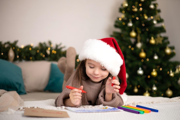 Feliz Natal e Boas Festas A garotinha feliz na cama escreveu uma carta para o Papai Noel e segura o envelope na mão