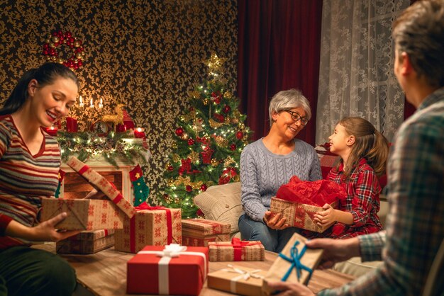 Feliz natal e boas festas! avó, mãe, pai e filho trocando presentes. pais e filha se divertindo perto de árvore dentro de casa. família amorosa com presentes no quarto.