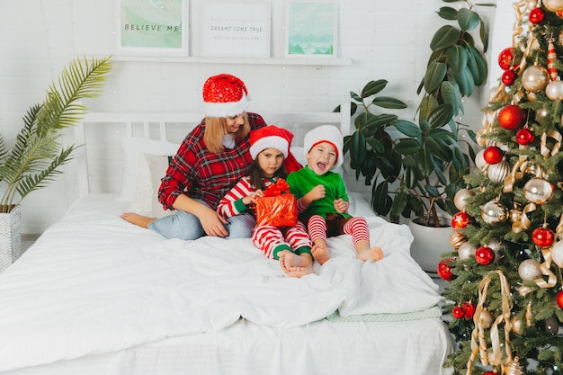 Feliz Natal e Boas Festas! Família feliz se divertir e brincar juntos na cama perto da árvore de Natal em casa. mãe e filhos estão se divertindo.
