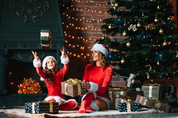 Feliz natal e boas festas! linda mãe com filha em fantasias de natal, passam algum tempo juntos perto da árvore de natal.