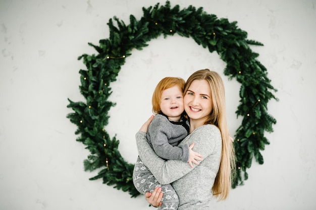 Feliz Natal e Boas Festas Mãe alegre abraçando filha bebê fofo perto da árvore de Natal Mãe e filho se divertindo e brincando juntos em casa