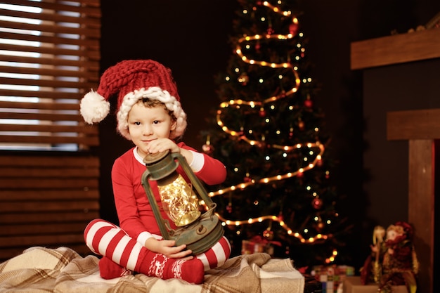 Feliz natal e boas festas um garotinho está sentado com uma lanterna na árvore de natal ano novo, elfo.