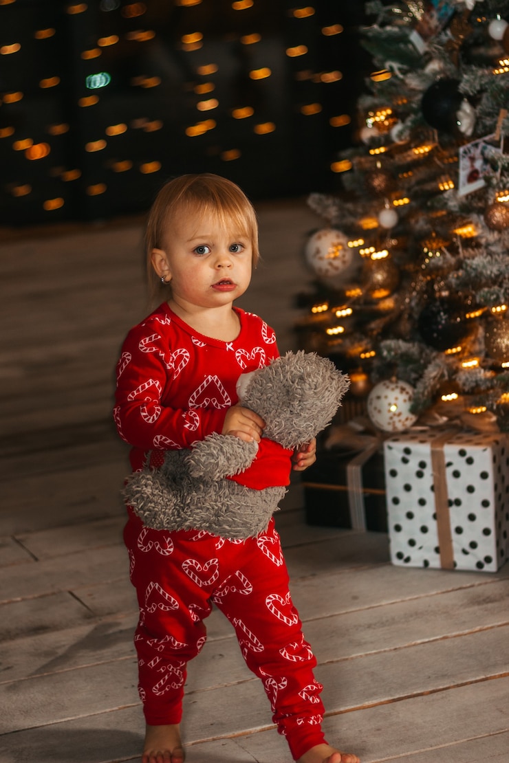 Foto feliz natal e boas festas. uma menina de pijama vermelho carrega um urso