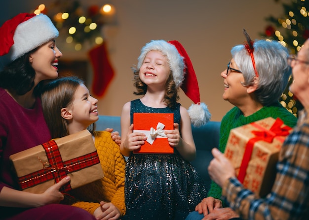 Feliz natal e boas festas! vovó, vovô, mãe e filhos trocando presentes. pais e filhas se divertindo perto de árvore dentro de casa. família amorosa com presentes no quarto.