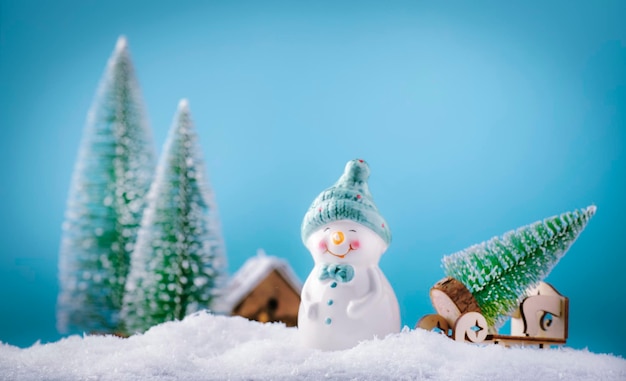 Feliz natal e feliz ano novo composição com espaço de cópia pequeno boneco de neve carrega árvore de natal da floresta de fadas para casa fundo festivo de inverno