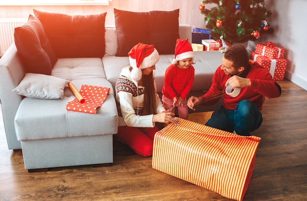 Feliz Natal e Feliz Ano Novo. Família sentada no chão perto de uma grande caixa de presentes