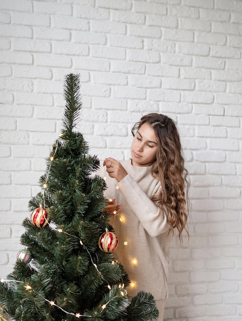 Feliz Natal e Feliz Ano Novo. jovem mulher atraente decorando a árvore de Natal com luzes de fada