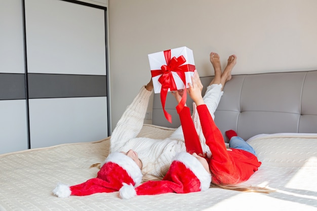 Foto feliz natal e feliz ano novo. mãe alegre e menina linda filha na cama. pai e filho