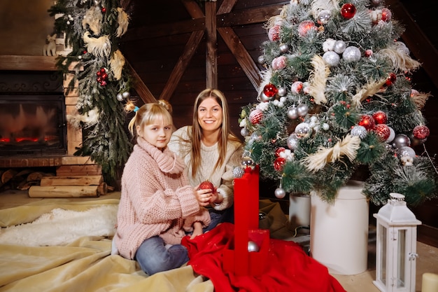 Feliz Natal e Feliz Ano Novo, mãe e filha decoram a árvore de Natal dentro de casa