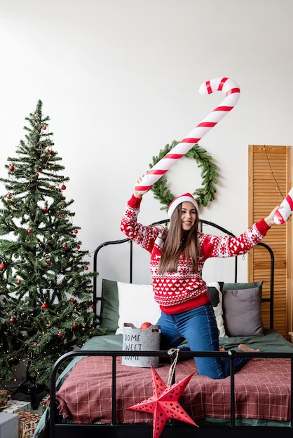 Feliz Natal e Feliz Ano Novo. Mulher jovem feliz com suéter vermelho e chapéu de Papai Noel dançando na cama celebrando o Natal