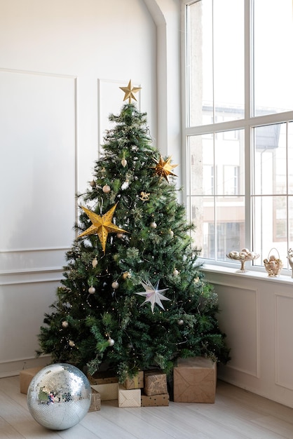 Feliz Natal e Feliz Ano Novo. Árvore de natal com presentes e luzes na sala bem iluminada e arejada ao lado da janela