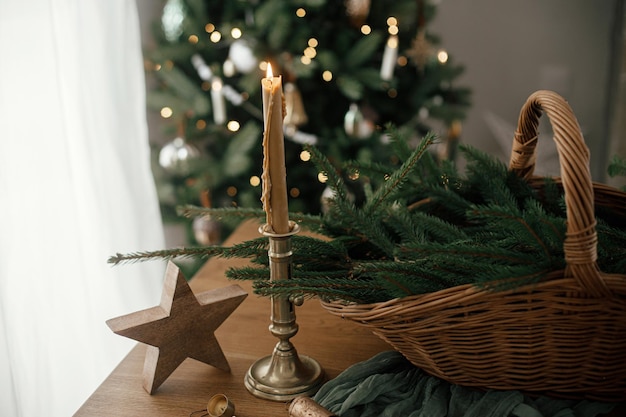 Feliz Natal e Felizes feriados Cesto rústico elegante com galhos de abeto vintage vela e estrela de madeira na mesa contra árvore de Natal decorada festiva na sala escandinava