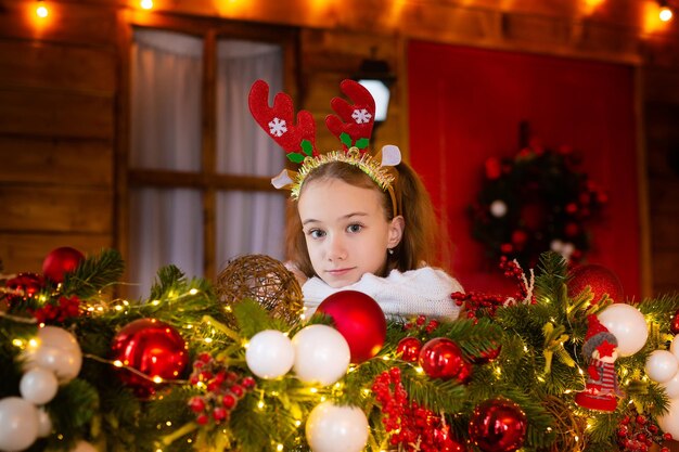 Feliz Natal e felizes feriados uma menina alegre com uma faixa de cabeça feita de chifres de veado ao lado do