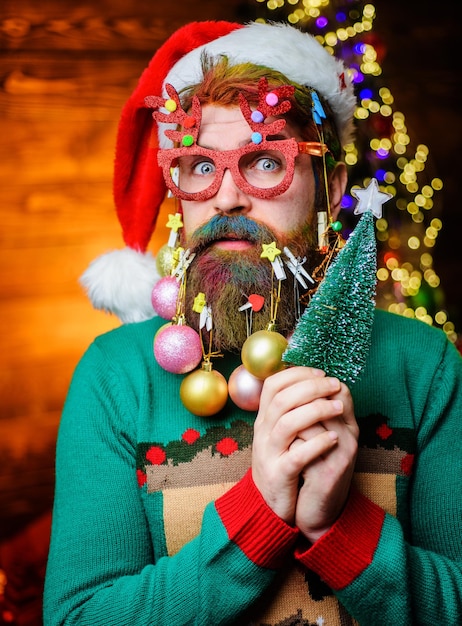 Feliz natal, feliz ano novo, homem barbudo com chapéu de papai noel e óculos de festa com uma pequena árvore de natal.