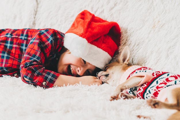 Feliz Natal feliz criança e cachorrinho com suéter brincando de abraço e se divertindo no sofá com