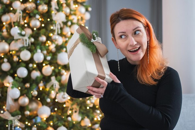 Feliz Natal mulher desempacotando abrir a caixa de presentes perto da árvore de Natal menina na sala de estar com