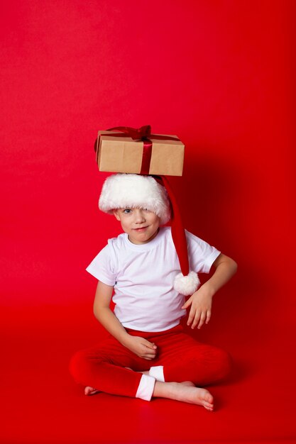 Feliz natal. retrato de um menino bonito em um boné de papai noel com caixas de presente em um fundo vermelho. um lugar para texto. foto de alta qualidade