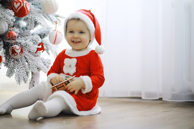 Feliz navidad brillante. Precioso bebé disfruta de la Navidad. Recuerdos de la infancia. Santa niña niño celebrar la Navidad en casa. Vacaciones familiares. Niña linda niño alegre juego de humor cerca del árbol de Navidad.