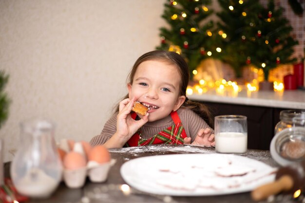 Feliz Navidad Una dulce y graciosa niña en una acogedora cocina decorada horneó galletas de Navidad y se las come Estilo de vida Tonos cálidos