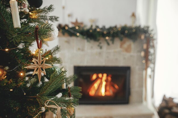 Feliz Navidad Elegantes adornos navideños en el árbol cerca de la chimenea ardiente Hermoso árbol de Navidad decorado con adornos antiguos, luces y cintas Ambiente navideño