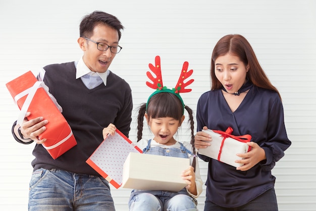 Feliz Navidad familia y alegres vacaciones. La madre y el padre sorprenden con los niños. Hija y padre que celebran el presente regalo en la sala de estar blanca.