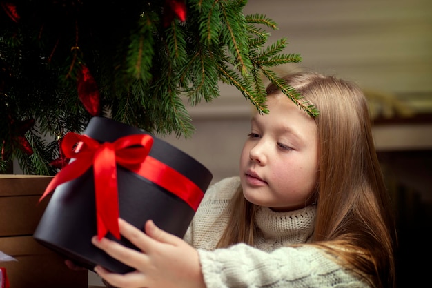 Feliz Navidad felices fiestas Alegre linda niña rubia abre un regalo de Navidad