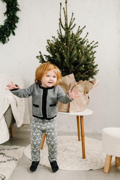 Feliz Navidad y Felices Fiestas Alegre niña linda cerca del árbol en la mañana