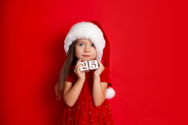 Feliz Navidad y felices fiestas Una chica divertida con sombrero de Papá Noel sostiene cubos con los números 25