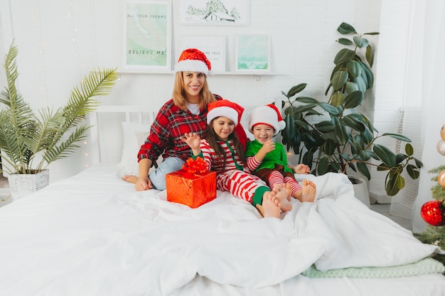 ¡Feliz Navidad y Felices Fiestas! La familia feliz se divierte y juega juntos en la cama cerca del árbol de Navidad en casa. mamá y los niños se divierten.