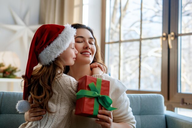 Feliz Navidad y Felices Fiestas Mamá alegre y su linda hija intercambiando regalos