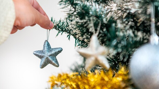 Feliz Navidad y felices fiestas, la mano de un hombre está decorando el abeto en el interior de la casa en invierno. Estrellas de Navidad colgando de ramas de abeto para banner de decoración, concepto de año nuevo.