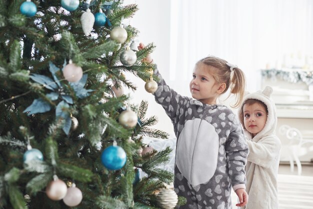 Feliz Navidad y felices fiestas! Niñas ayudando a decorar el árbol de Navidad, sosteniendo algunas bolas de Navidad en la mano.