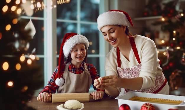 Foto feliz navidad y felices fiestas preparación familiar de comida navideña madre e hija cocinando pastel