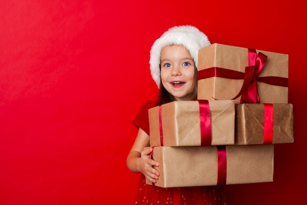 Feliz Navidad y felices fiestas Retrato de niña emocional en una gorra de Santa sobre un fondo rojo.