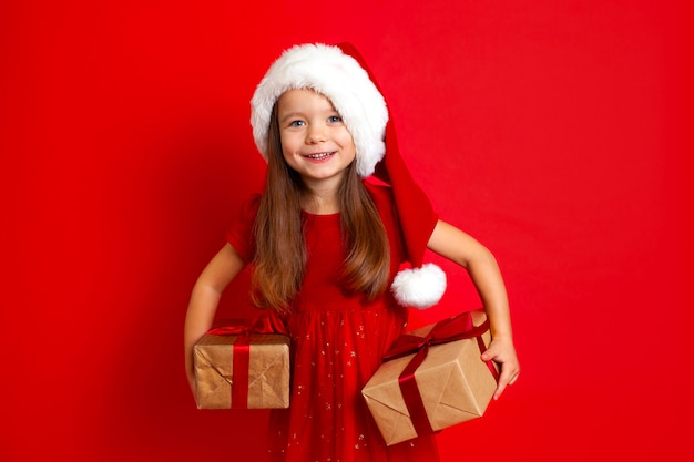 Feliz Navidad y felices fiestas Retrato de niña emocional en una gorra de Santa sobre un fondo rojo.