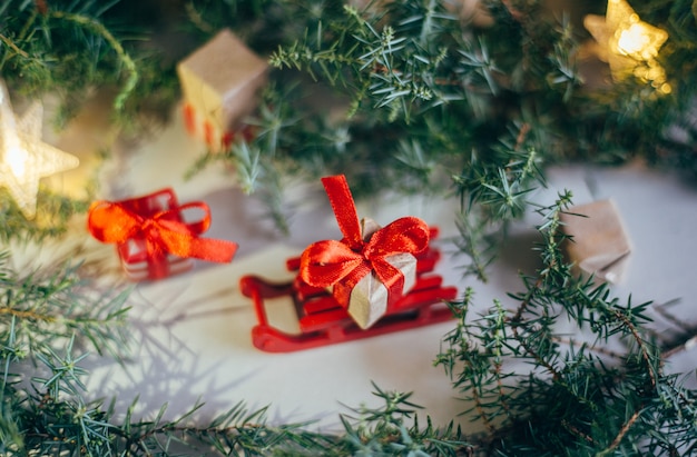 Feliz Navidad y felices fiestas tarjeta de felicitación, marco, banner. Año Nuevo 2020. Ramas de los árboles de hoja perenne. Caja de regalo de Navidad en trineos de madera. Caja con una cinta roja.