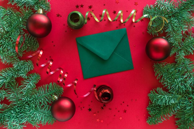 Feliz Navidad feliz año nuevo concepto. Composición navideña. Carta de Navidad, adornos, ramas de abeto en superficie roja. Vista superior, endecha plana.