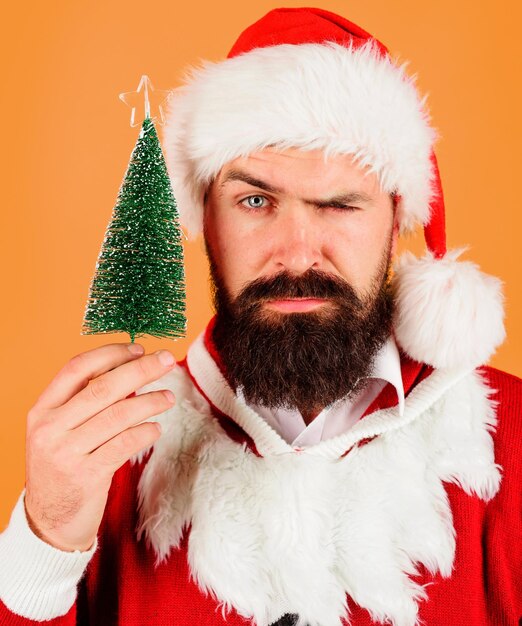 Feliz Navidad y Feliz Año Nuevo hombre barbudo serio en traje de Papá Noel con pequeño árbol de Navidad