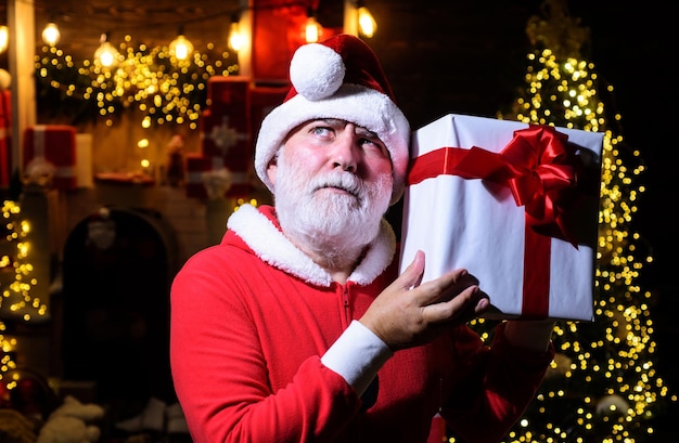 Foto feliz navidad y feliz año nuevo pensativo papá noel con regalo de navidad pensativo hombre barbudo